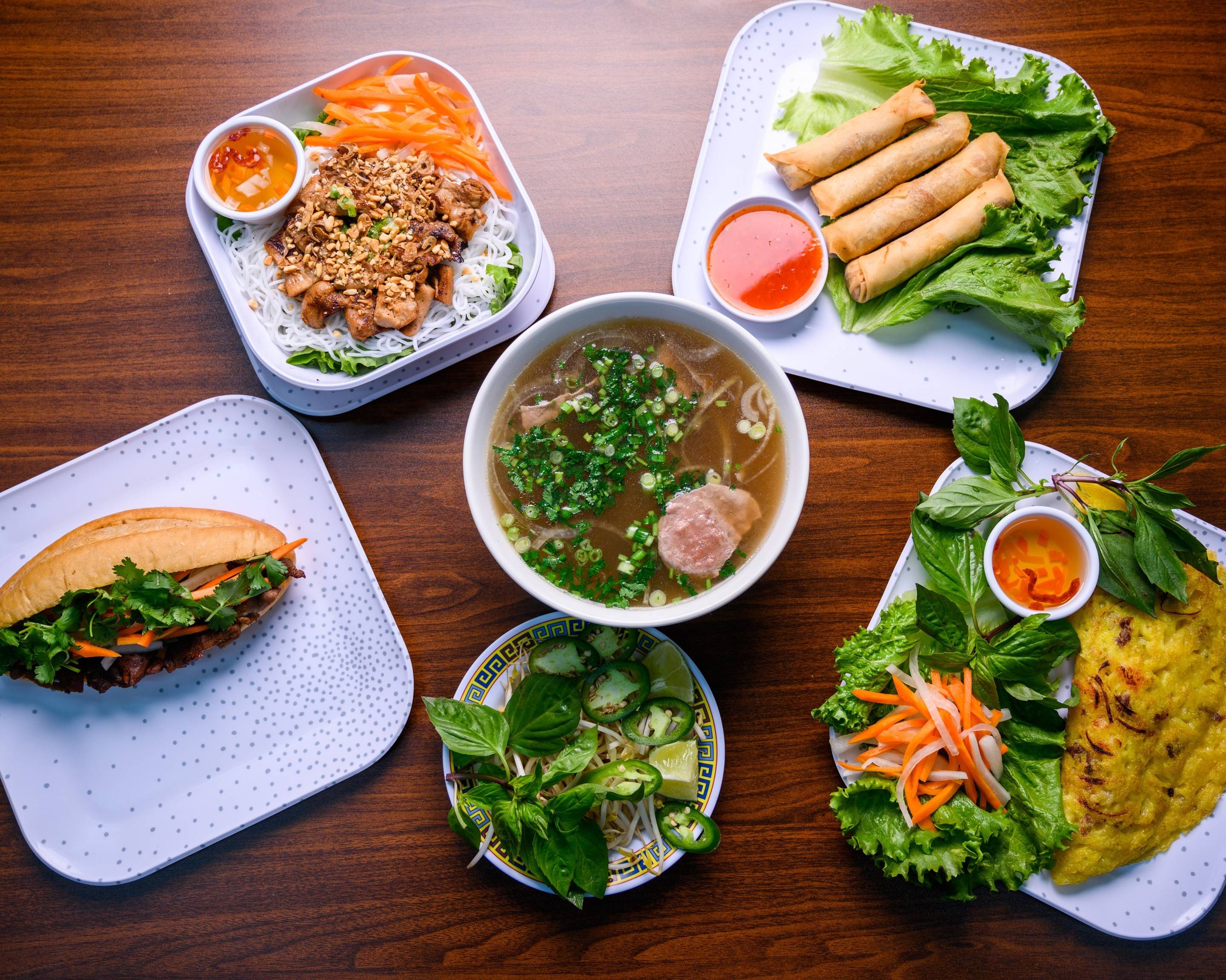 Vietnamese Food Table that includes Pho Noodle Soup, bun thit nuong, cha gio springroll, banh xeo, and bánh mì sandwich